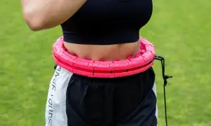 Kobieta w sportowym topie i spodenkach ćwiczy z różową obręczą. Efektywny trening silowy dla kobiet.