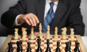 Mężczyzna w garniturze, jak prawdziwy **grandmaster**, przygotowuje się do partii szachów. Na planszy czarne figury czekają na ruch.