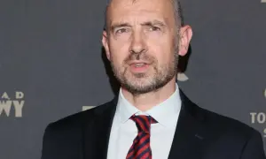 Mężczyzna w garniturze i krawacie, z siwiejącymi włosami. Wygląda jak trener siatkówki mężczyzn, gotowy do analizy gry.