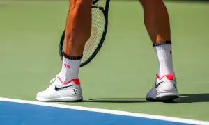 Widok na łydkę tenisisty w białych skarpetkach i butach Nike, gotowego do uderzenia.