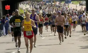 Uczestnicy biegną w maratonie, zastanawiając się, ile trwa maraton. Widać zawodników z numerami startowymi, kibiców i most nad trasą.