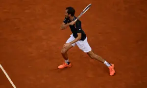 Tenisista wykonuje potężny **backhand** na ceglanej nawierzchni.