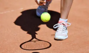 Tenisista przygotowuje się do uderzenia piłki. Cień rakiety i piłki na korcie przypomina, co to ATP.