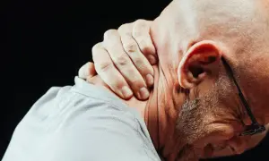 Mężczyzna masuje kark, odczuwając ostry ból szyi przy skręcaniu głowy.