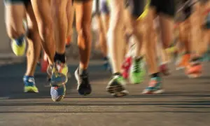 Nogi biegaczy w ruchu, niektórym po bieganiu grozi biegunka. Kolorowe buty sportowe na asfalcie.