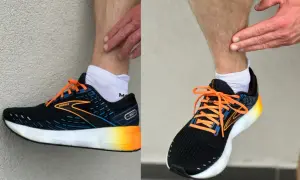 Biegacz pokazuje ból w łydce, który może być objawem shin splints. Na nogach ma czarne buty sportowe Brooks z pomarańczowymi sznurówkami.
