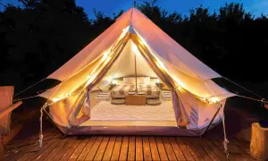 Glamping co to? Luksusowy namiot z wygodnym łóżkiem, oświetlony girlandą świateł, na drewnianym tarasie.