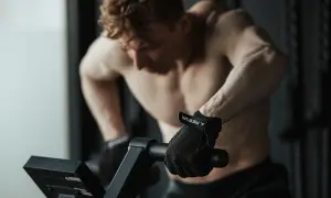 Mężczyzna w rękawiczkach ćwiczy cardio na rowerze stacjonarnym, skupiony na treningu.