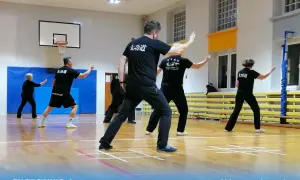 Grupa ćwiczy tai chi w sali gimnastycznej. Wszyscy mają czarne stroje. Warto pamiętać o tai chi przeciwwskazania, choć ćwiczenia są łagodne.
