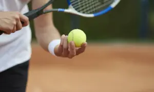Gracz trzyma piłkę do tenisa ziemnego, gotowy do serwisu. Poznaj zasady gry w tenisa ziemnego i zacznij grać!