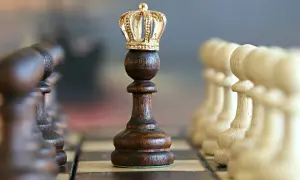 Szachownica z figurami. Centralnie ustawiony ciemny pionek z koroną, symbolizujący gambit królowej.