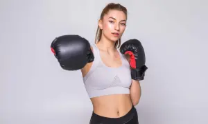 Młoda kobieta w sportowym topie i legginsach, w rękawicach bokserskich, ćwiczy w domu.