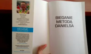 Otwarta książka z hasłem "Bieganie metodą Danielsa" na prawej stronie. Na lewej stronie zdjęcie biegacza i opis jego osiągnięć.
