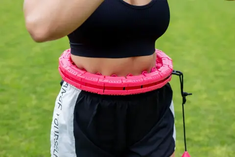 Kobieta w sportowym topie i spodenkach ćwiczy z różową obręczą. Efektywny trening silowy dla kobiet.