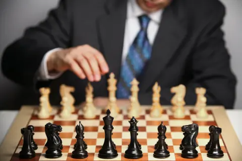 Mężczyzna w garniturze, jak prawdziwy **grandmaster**, przygotowuje się do partii szachów. Na planszy czarne figury czekają na ruch.