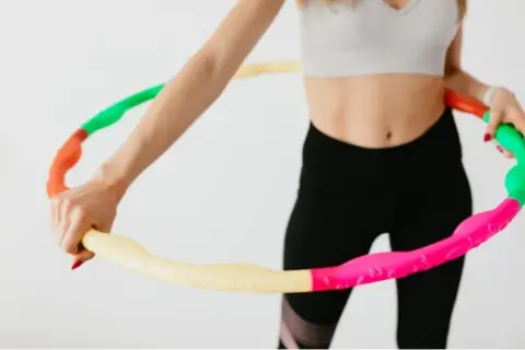 Kobieta w sportowym stroju trzyma kolorową obręcz hula hop. Czy hula hop jest szkodliwe? Nie, to świetna zabawa i trening!
