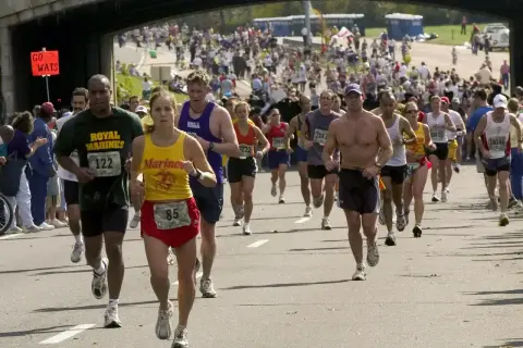 Uczestnicy biegną w maratonie, zastanawiając się, ile trwa maraton. Widać zawodników z numerami startowymi, kibiców i most nad trasą.