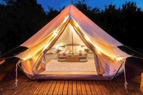 Glamping co to? Luksusowy namiot z wygodnym łóżkiem, oświetlony girlandą świateł, na drewnianym tarasie.
