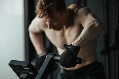 Mężczyzna w rękawiczkach ćwiczy cardio na rowerze stacjonarnym, skupiony na treningu.