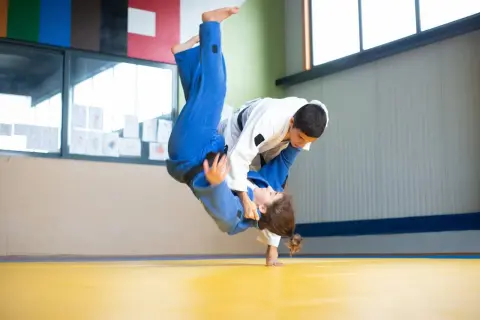 Dynamiczny rzut w judo, zawodniczka w niebieskim kimonie leci w powietrzu, grożąc nokautem w judo.