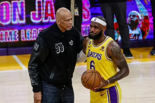 Kareem Abdul-Jabbar rozmawia z LeBronem Jamesem, który trzyma piłkę. Obaj są legendami NBA, a LeBron niedawno pobił rekordy punktowe.