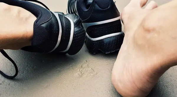 Czarne buty sportowe i bosa stopa na ziemi. Czas na trening, nawet jeśli paznokcie biegacza dają o sobie znać.
