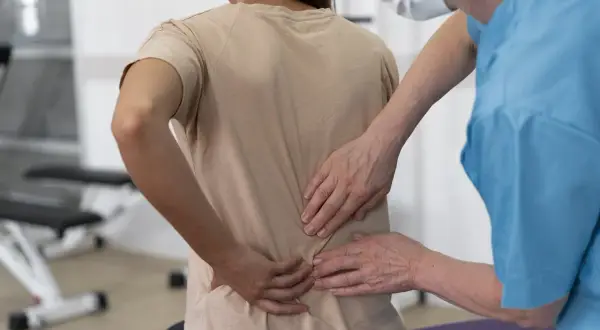 Fizjoterapeuta bada pacjentkę z bólem w odcinku lędźwiowym kręgosłupa, który mógł powstać po upadku.