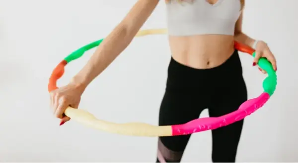 Kobieta w sportowym stroju trzyma kolorową obręcz hula hop. Czy hula hop jest szkodliwe? Nie, to świetna zabawa i trening!