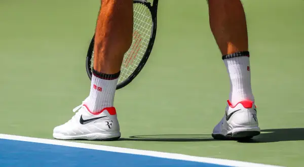 Widok na łydkę tenisisty w białych skarpetkach i butach Nike, gotowego do uderzenia.