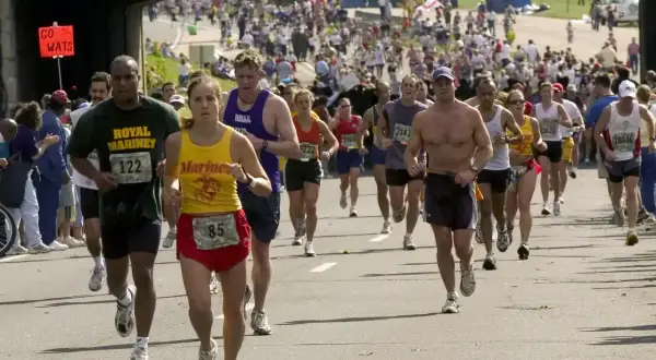 Uczestnicy biegną w maratonie, zastanawiając się, ile trwa maraton. Widać zawodników z numerami startowymi, kibiców i most nad trasą.