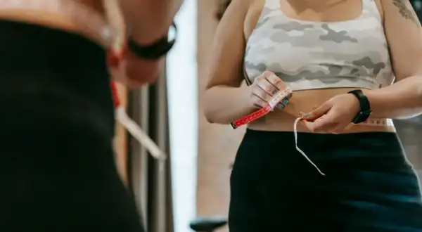 Kobieta mierzy talię centymetrem. Codzienne chodzenie 5 km dziennie efekty widać w obwodach.