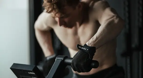Mężczyzna w rękawiczkach ćwiczy cardio na rowerze stacjonarnym, skupiony na treningu.