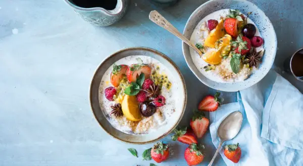 Dwa talerze owsianki z owocami (truskawki, maliny, pomarańcza, marakuja) i gwiazdkami anyżu. Idealne na śniadanie w stylu dieta wysokowęglowodanowa.