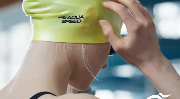 Dziewczyna zakłada jaskrawożółty czepek na basen z logo Aqua Speed.