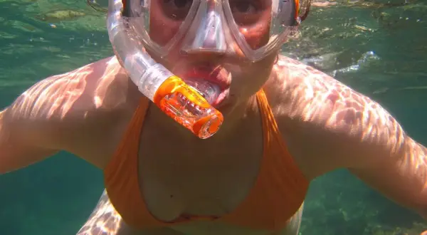Kobieta w masce i rurce do snorkelingu, zanurzona w turkusowej wodzie, cieszy się podwodnym światem.