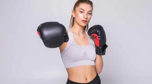 Młoda kobieta w sportowym topie i legginsach, w rękawicach bokserskich, ćwiczy w domu.