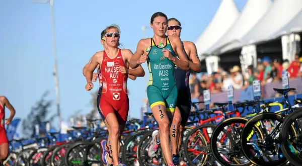 Trzy zawodniczki biegną w zawodach triathlonowych. To dyscyplina łącząca pływanie, jazdę na rowerze i bieg.