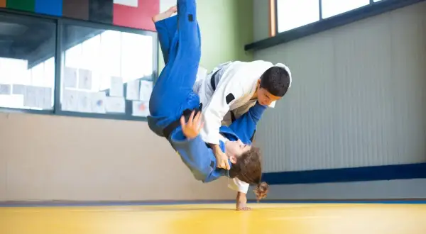 Dynamiczny rzut w judo, zawodniczka w niebieskim kimonie leci w powietrzu, grożąc nokautem w judo.