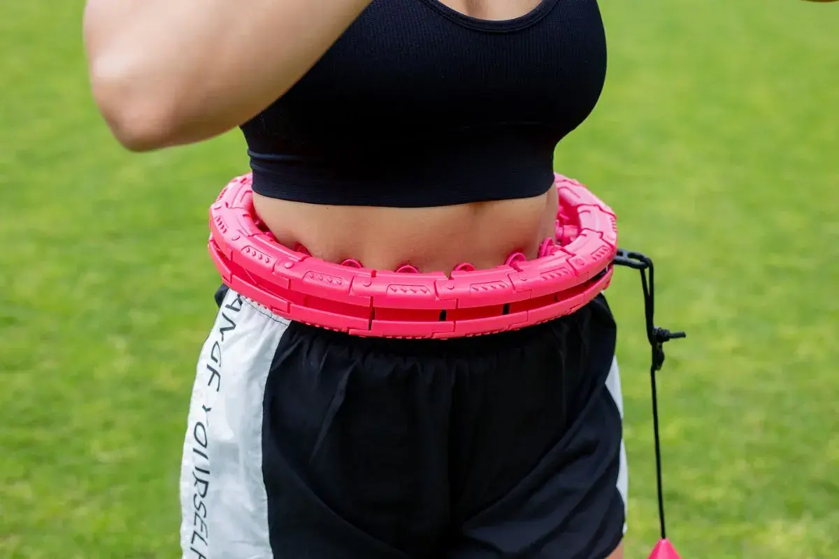 Kobieta w sportowym topie i spodenkach ćwiczy z różową obręczą. Efektywny trening silowy dla kobiet.