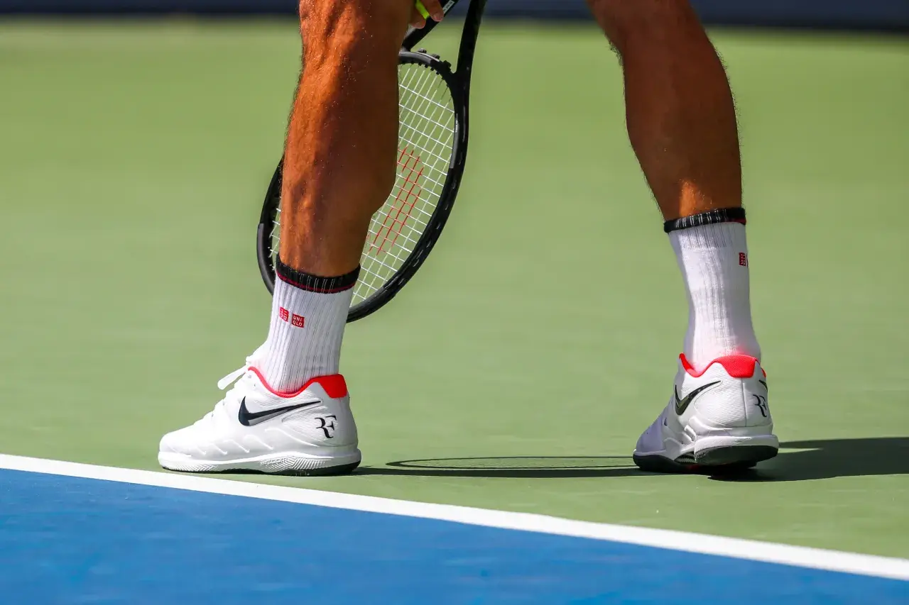 Widok na łydkę tenisisty w białych skarpetkach i butach Nike, gotowego do uderzenia.