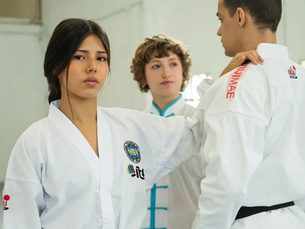 Trójka młodych ludzi w białych strojach do taekwondo, jednej z najpopularniejszych sztuk walki, ćwiczy w sali treningowej.