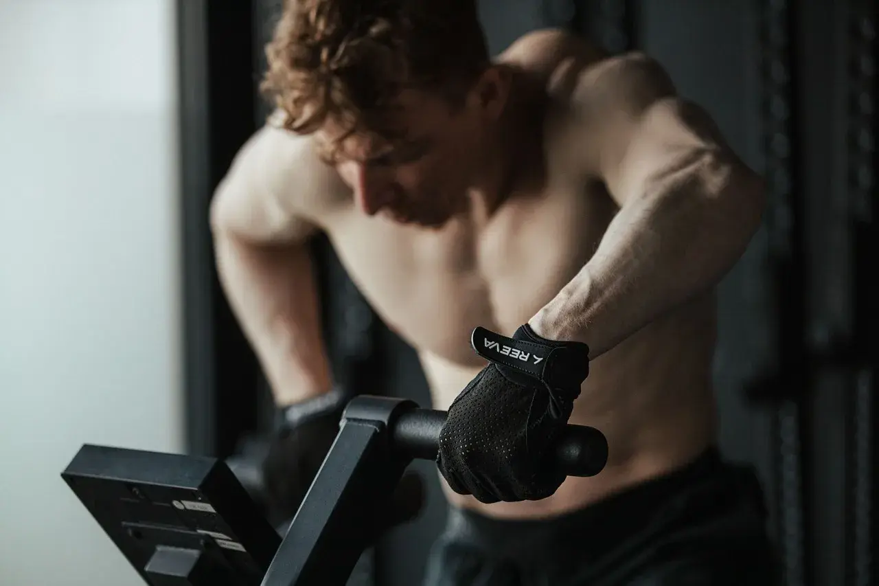 Mężczyzna w rękawiczkach ćwiczy cardio na rowerze stacjonarnym, skupiony na treningu.