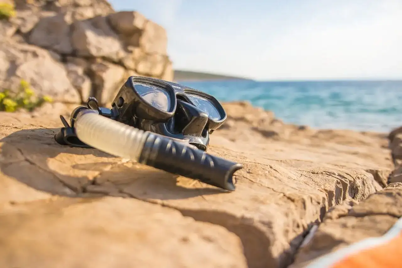 Maska i fajka do snorkelingu leżą na kamienistej plaży. To sprzęt, który pozwala odkrywać podwodny świat.