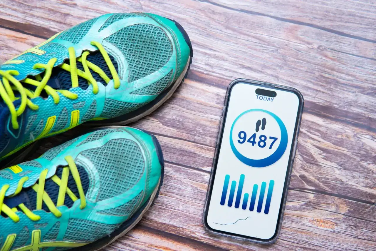 Buty sportowe i telefon z aplikacją pokazującą 9487 kroków. Czy to odpowiedź na pytanie, ile kroków dziennie powinno się robić?