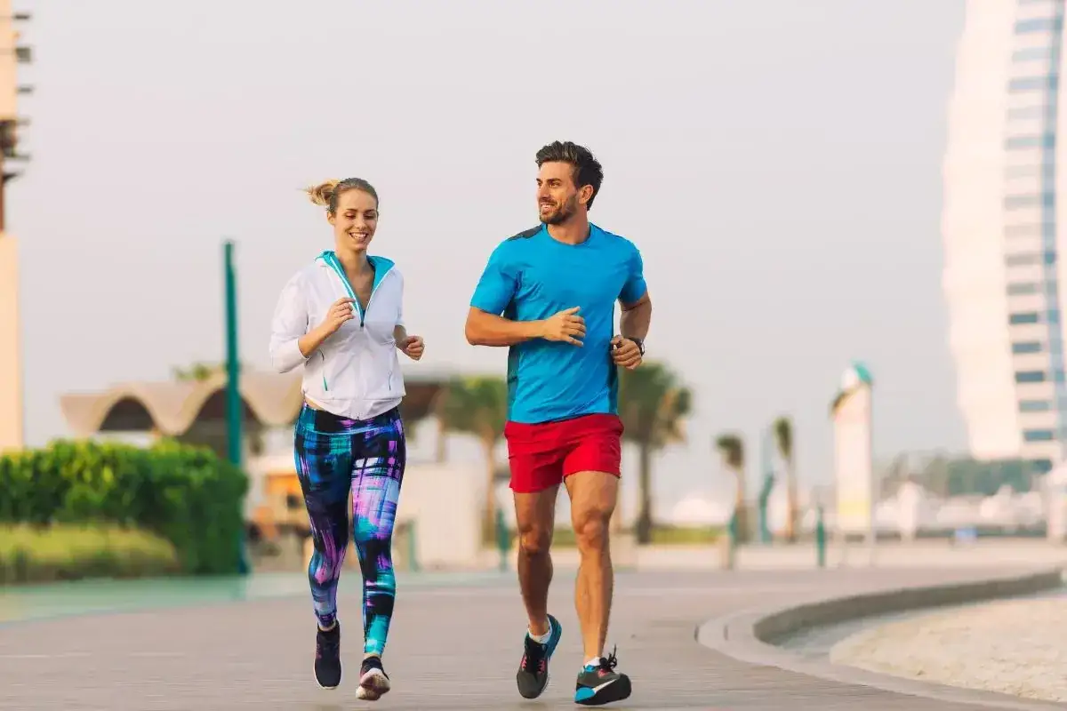 Para biegnie w słońcu. Ona w kolorowych legginsach, on w czerwonych spodenkach. Cieszą się wspólnym, spokojnym slow joggingiem wzdłuż plaży.