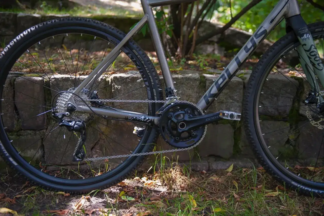 Szary rower gravelowy Kellys Soot z napędem Shimano GRX, jeden z wielu rodzajów rowerów, gotowy na przygodę.