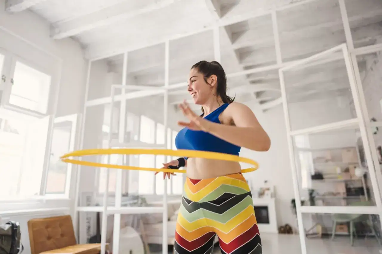 Uśmiechnięta kobieta kręci żółtą obręczą hula hop. Czy hula hop jest szkodliwe? Nie, to świetna zabawa i trening!