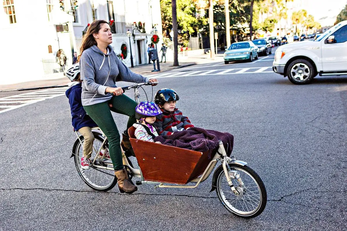 Mama z dwójką dzieci na rowerze cargo. To świetny przykład, jak dobrac rower dla dziecka, gdy potrzebujemy przewieźć więcej niż jedno.