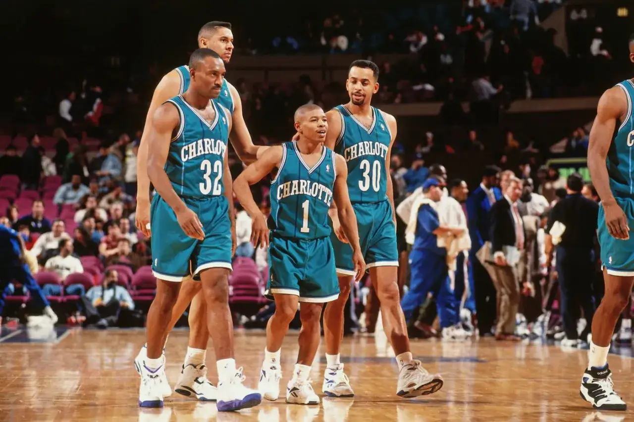 Koszykarze Charlotte Hornets, w tym najniższy koszykarz NBA, w turkusowych strojach na parkiecie.