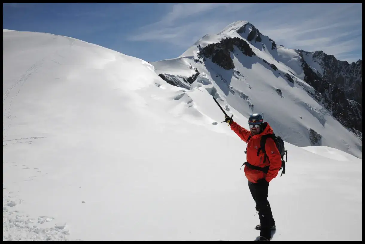 Wspinacz w pomarańczowej kurtce wskazuje na ośnieżone szczyty. Zastanawiasz się, ile kosztuje wejście na Mont Blanc?